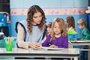 Teacher And Girl Reading Book With Children In Background