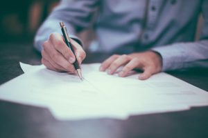 homme qui écrit sur du papier avec un stylo